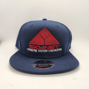 May include: A navy blue baseball cap with a red embroidered logo that says "SKYNET CYBERDYNE SYSTEMS CORPORATION".