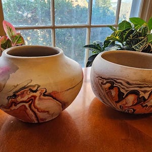 May include: Two ceramic pots with a marbled design in shades of brown, white, and orange. The pots are on a wooden surface.
