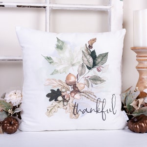 May include: White cushion with a watercolour design of autumn leaves, acorns, and the word "thankful" in black script.