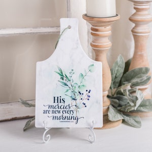 May include: White marble chopping board with a watercolour design of green leaves and blue berries. The board has a white stand and the text "His mercies are new every morning - Lamentations 3:23"