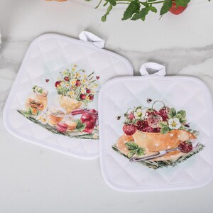 May include: Two white quilted pot holders with a strawberry and floral design. One pot holder features a bowl of strawberries, the other has a jar of honey and flowers. Strawberries are in a white bowl.