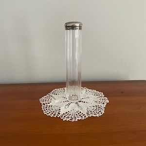 May include: A clear glass jar with a silver lid. The jar has a ribbed design and is sitting on a white crocheted doily.