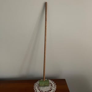 May include: A wooden mallet with a green head, resting on a white crocheted doily. The mallet has a long wooden handle.