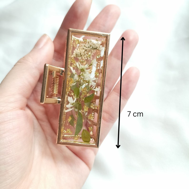 Pu&ograve; includere: Fermaglio per capelli dorato con una cornice rettangolare che contiene fiori bianchi pressati e glitter dorato. Il fermaglio misura 7 cm di lunghezza.