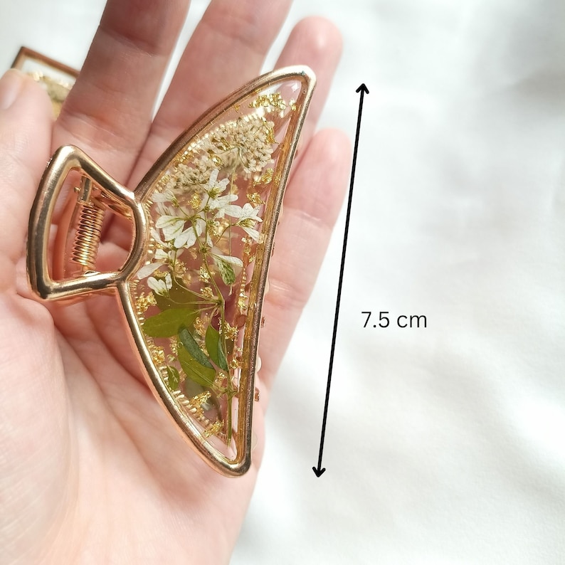 Pu&ograve; includere: Fermaglio per capelli dorato a forma di mezzaluna con un design di fiori bianchi pressati e foglia d'oro. Il fermaglio &egrave; lungo 7,5 cm.