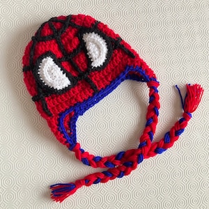 May include: A red and black crocheted hat with a spider-man design. The hat has a long blue and red braided tail.