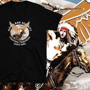 Puede incluir: Camiseta negra con un gráfico de un águila que lleva a un guerrero nativo americano. El gráfico está rodeado por un círculo con el texto "Homeland Security Fighting Terrorism Since 1492".