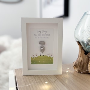 May include: White framed picture with a motivational quote, "Stay Strong Make them wonder how you're still smiling."  The quote is accompanied by a pebble art illustration of a smiling figure lifting a weight.