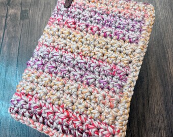 May include: A rectangular, hand-crocheted case in a mix of colors including pink, purple, yellow, and white. The case has a leather tag with the text "leandloops" attached to the top. The stitches are tight and even, creating a textured surface.