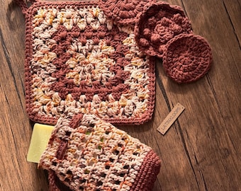 May include: A set of crocheted items including a square washcloth, three round facial pads, and a rectangular soap pouch containing a light yellow bar of soap. The items feature a variegated yarn in shades of terracotta, cream, and brown. A small wooden tag is engraved with the text LATINXLOOPS.