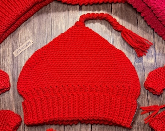 May include: A vibrant red knitted hat with a tassel, surrounded by matching accessories. The hat has a unique shape and texture, suggesting handmade craftsmanship. The image is set against a wooden background, showcasing the hat's color and design. The brand name "LATINXLOOPS" is visible.