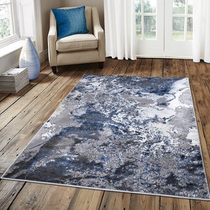May include: A blue and grey abstract area rug with a marbled design. The rug is on a hardwood floor in a living room setting.
