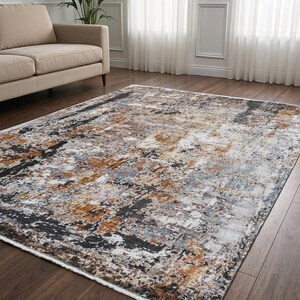 May include: A rectangular area rug featuring an abstract pattern with a distressed, weathered appearance. The design incorporates a blend of deep black, warm copper, burnt orange, soft grey, and cream white tones across the entire surface.