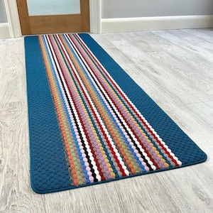 May include: A teal hallway runner with a textured surface and a central stripe pattern of vertical lines in various colours. The rug is designed for a hallway or entryway.