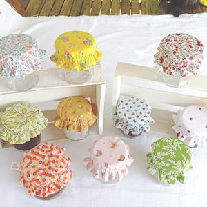 Peut inclure: Neuf couvercles en tissu pour bocaux dans différents motifs et couleurs. Les couvercles sont en tissu de coton et ont un bord festonné. Les bocaux ne sont pas visibles.