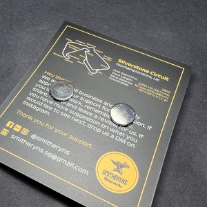 May include: A black and white image of the Silverstone Circuit race track in Northamptonshire, UK. The image includes the track layout, the name of the circuit, and the location. The text also includes the date of the first Grand Prix, the track length, the race distance, and the coordinates of the circuit. The image also includes two silver metal magnets.