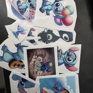 May include: A collection of colorful stickers featuring the character Stitch from the animated film Lilo & Stitch. The stickers depict Stitch in various poses, including holding balloons, surfing, and on a planet. The stickers are on a black surface.