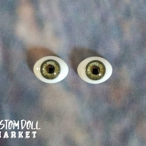 Può includere: Due occhi di bambola con iride verde chiaro e pupilla nera. Gli occhi sono di forma ovale con sclera bianca. Il testo "CUSTOM DOLL MARKET" è stampato in bianco in basso nell'immagine.