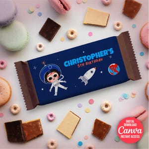 Könnte beinhalten: Dunkelblaue Schokoriegelverpackung mit dem Text "CHRISTOPHER'S 5TH BIRTHDAY" und Illustrationen eines Astronauten, einer Rakete und eines Planeten. Die Verpackung ist von Süßigkeiten umgeben, darunter Macarons, Schokoriegel und Donuts.