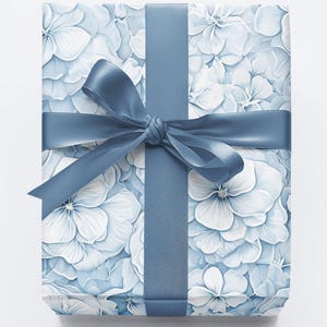 Puede incluir: Un regalo envuelto en papel con un estampado de flores de hortensia blancas y azul claro. Una cinta y un lazo azules a juego adornan el regalo. La imagen sugiere un tema de celebraci&oacute;n y regalos, adecuado para diversas ocasiones.