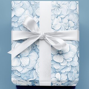 Puede incluir: Un regalo envuelto con un estampado floral de flores de hortensia blancas y azul claro. El regalo est&aacute; atado con una cinta y un lazo blancos, sobre un fondo azul claro.