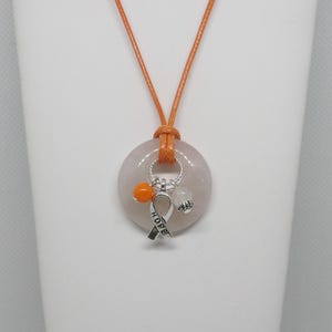 May include: A rose quartz pendant necklace with an orange cord. The pendant has a circular shape with a silver charm that says "HOPE" and two small beads. The necklace is displayed on a white surface.