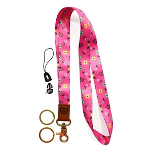 May include: A pink lanyard with a floral pattern, a gold key ring with two rings, and a black phone charm with a clip.
