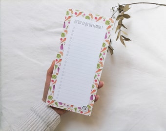 Puede incluir: Un bloc de notas blanco con un interior rayado y un borde de verduras coloridas. El bloc de notas tiene el texto "Qu'est-ce qu'on mange?" impreso en la parte superior.