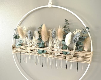 May include: A white metal hoop with a woven base decorated with dried flowers and greenery. The flowers are in shades of white, beige, and brown. The greenery is a light green.
