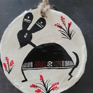 May include: A white ceramic ornament with a black rabbit design and red flower accents. The rabbit has a geometric pattern on its body and is standing on its hind legs.