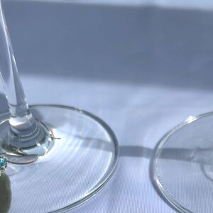 May include: Four silver wine glass charms with gray stone pendants and colorful beads. The charms are hanging from the stems of wine glasses.
