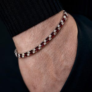 May include: A gold bracelet with alternating rectangular red gemstones and small white gemstones. The bracelet is worn on a wrist, with a black background.