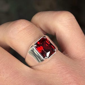 Puede incluir: Un anillo de plata con una piedra roja cuadrada grande.