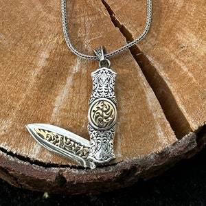 May include: A silver chain necklace with a silver and gold pocket knife pendant. The knife is open and has intricate details.