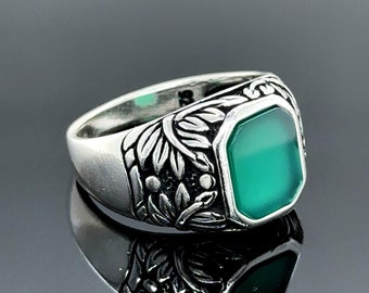 May include: A silver ring with a green gemstone set in a detailed floral design.