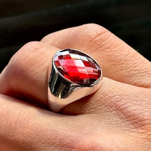 May include: A silver ring with a large, red, faceted gemstone.
