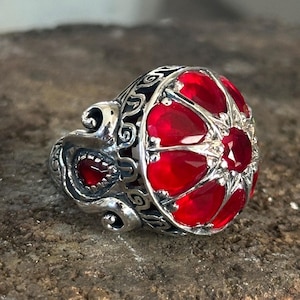 May include: A silver ring with a large red gemstone set in a detailed, ornate design.