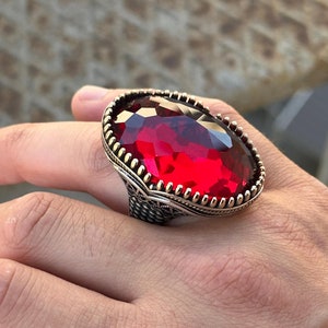 May include: A silver ring with a large, oval-shaped, red gemstone set in a decorative, ornate silver setting.