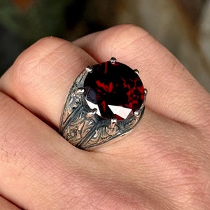 May include: A silver ring with an ornate design and a large, red gemstone.