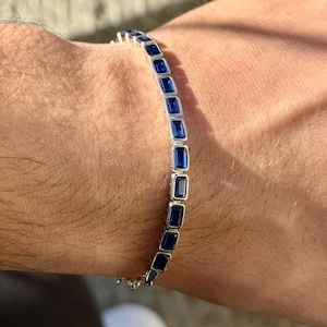 Puede incluir: Una pulsera de plata con piedras preciosas rectangulares de color azul oscuro. La pulsera está en una muñeca, con las piedras dispuestas en fila. Una joya delicada.