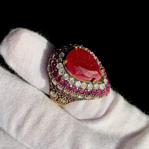 May include: A silver ring with a large red pear-shaped gemstone surrounded by smaller clear and pink gemstones.