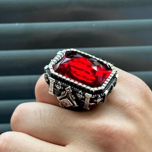 May include: A silver ring with a large, red, faceted gemstone set in a detailed, ornate design.