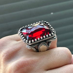 May include: A silver ring with a large, red, faceted gemstone set in a detailed, ornate design.