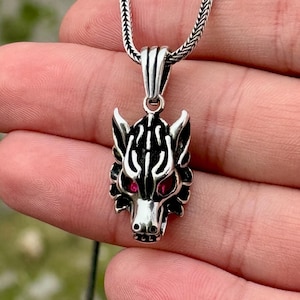 May include: Silver chain necklace with a wolf head pendant. The pendant is detailed with black and silver accents and has red eyes.