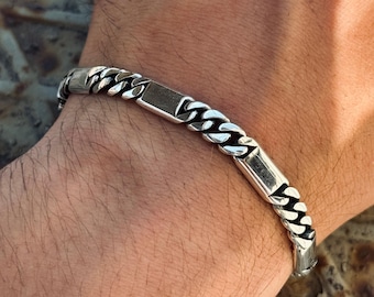May include: A silver chain bracelet with rectangular links and a curb chain design. The bracelet is worn on a wrist and has a polished finish. The jewelry is a stylish accessory.