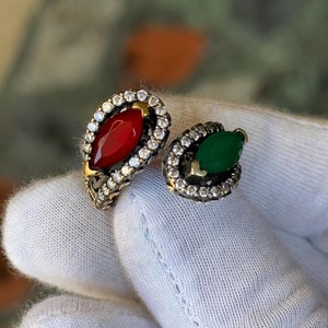 May include: Two silver rings with red and green gemstones surrounded by clear cubic zirconia stones.