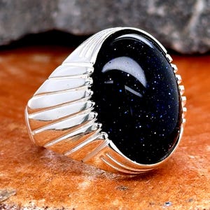 Op de afbeelding: Een zilveren ring met een donkerblauwe, ovale edelsteen. De ring heeft een getextureerde band met een gegroefd ontwerp.