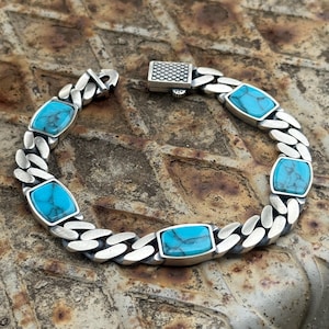 Peut inclure: Un bracelet en argent orné de pierres turquoise. Le bracelet présente un motif de chaîne gourmette avec des pierres turquoise rectangulaires serties dans des lunettes en argent. Le fermoir est un carré texturé.