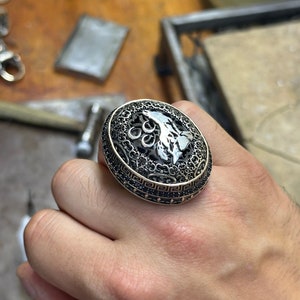 Op de afbeelding: Een zilveren ring met een zwart filigraanontwerp en een motief van een halve maan en een ster. De ring is bezet met zwarte stenen.