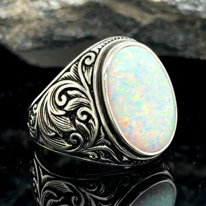 May include: A silver ring with an oval-shaped opal gemstone. The ring has a detailed floral design.